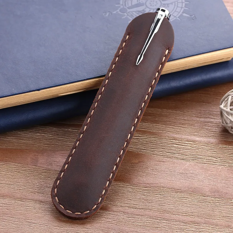 Dark brown leather pen holder with a pen on a wooden surface