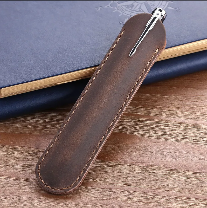 Brown leather pen holder with a pen on a wooden surface
